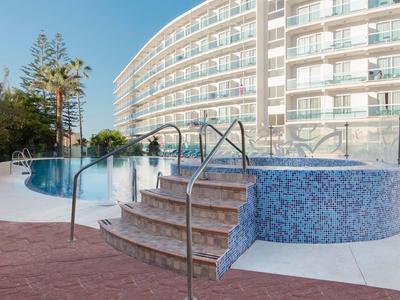 Venkovní bazén s vířivkou vedle vícepatrového hotelu s balkony