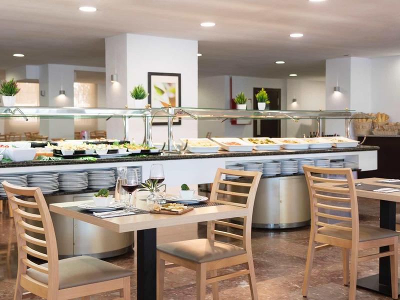 Moderner Buffetbereich mit Holzstühlen, gedeckten Tischen und verschiedenen Speisen auf weißen Platten.