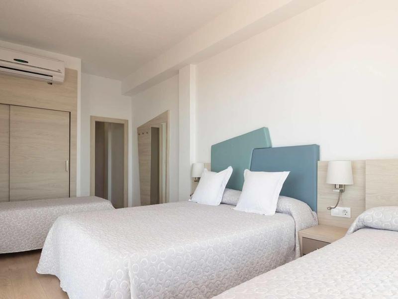 Drei Betten im hellen, modernen Schlafzimmer mit weißen Wänden und blau-grauen Kopfstützen.