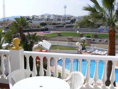 Vue depuis un balcon avec balustrade blanche sur une piscine et un terrain de sport par temps ensoleillé