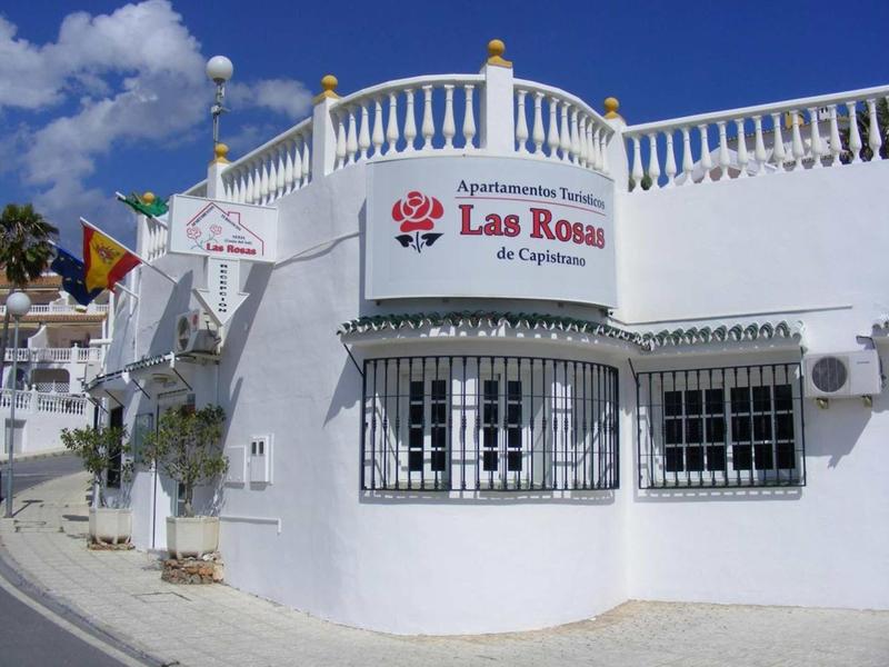 Weißes Gebäude mit geschwungenem Balkon und Schild "Las Rosas" unter blauem Himmel.
