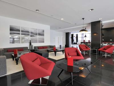 Moderner Hotel-Lounge-Bereich mit roten Sesseln und grauen Sofas auf schwarzem Boden.