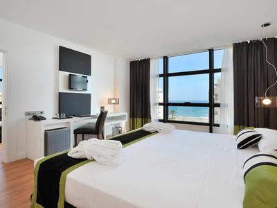 Modernes Hotelzimmer mit großem Bett, Fensterfront und Meerblick.