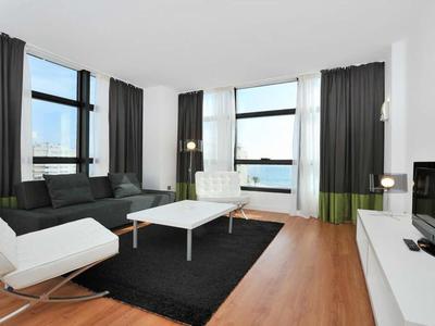 Modern eingerichtetes Wohnzimmer mit weißen Sitzmöbeln, Holzfußboden und großen Fenstern mit Blick aufs Meer.