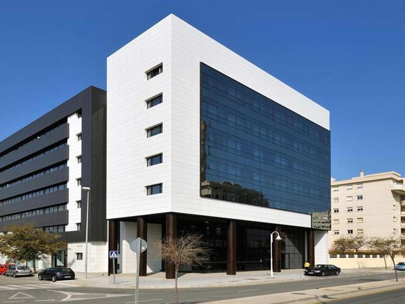 Modernes Bürogebäude mit großer Glasfassade, weiß-schwarzer Struktur und klarem blauen Himmel.