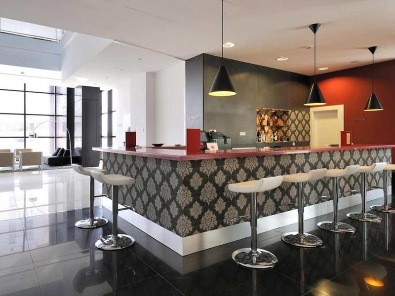 Moderner Barbereich mit grauem gemustertem Tresen, weißen Barhockern und großen Fenstern.