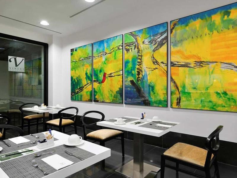 Modernes Restaurant mit weißen Tischen, schwarzen Stühlen und buntem vierteiligem Wandbild.