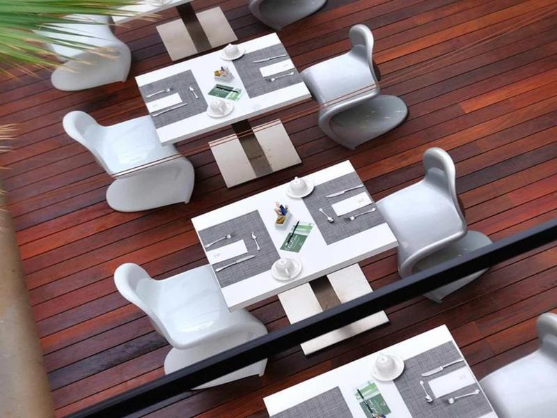 Vier gedeckte Tische mit weißen Stühlen auf dunklem Holzboden, von oben und spiegelnd fotografiert.