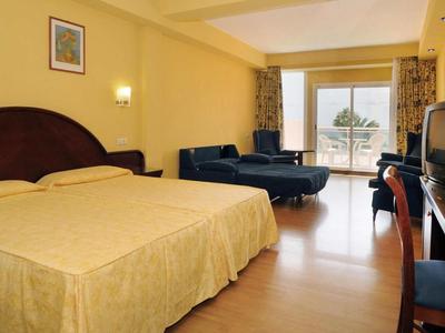 Hotelzimmer mit Doppelbett, Sesseln, Schreibtisch und Blick auf Terrasse mit Meer