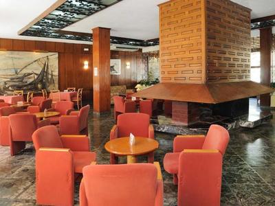 Gemütlicher Hotel-Loungebereich mit roten Sesseln und Kamin in der Mitte.