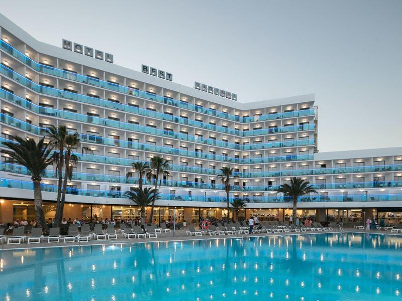 Moderner Hotelkomplex mit dreckigem Außenpool, beleuchteten Zimmern und Palmen bei Dämmerung.