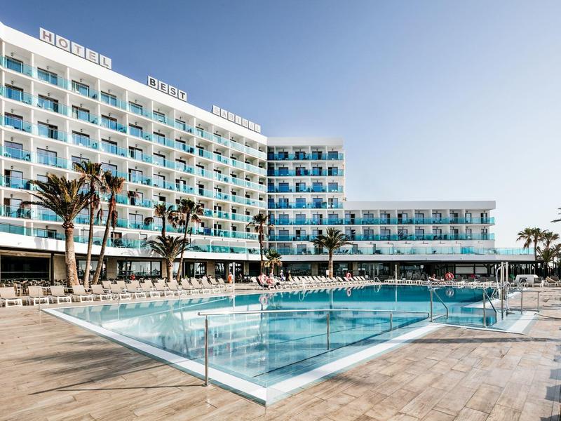 Modernes Hotel mit Blautönen, großem Pool und Sonnenterrasse, umgeben von Palmen und klarem Himmel.