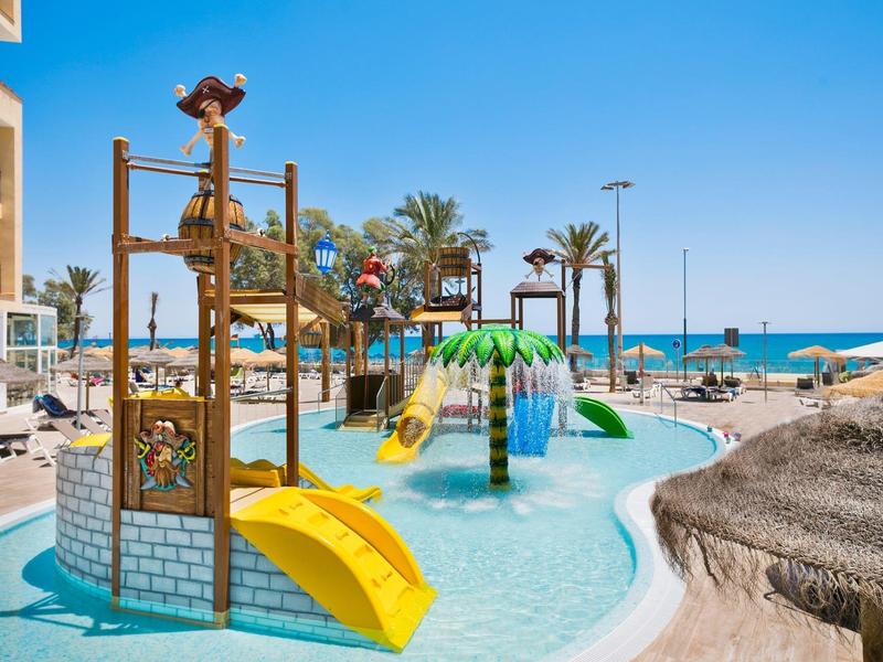 Kinderwasserspielplatz mit kleinen Rutschen und Klettergeräten am Strand unter blauem Himmel.