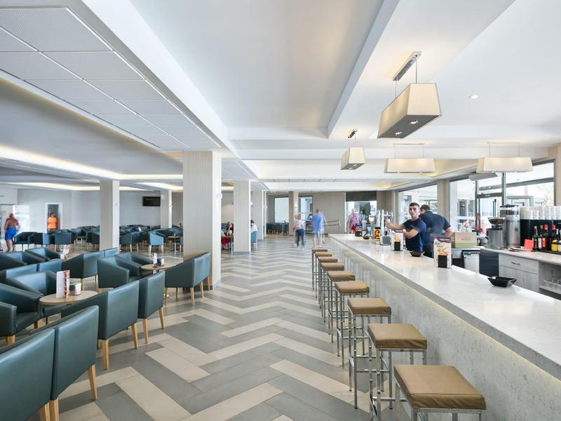 Helle Bar mit Ledersesseln, Holzhockern, langen Theken und moderner Beleuchtung in großzügigem Raum.