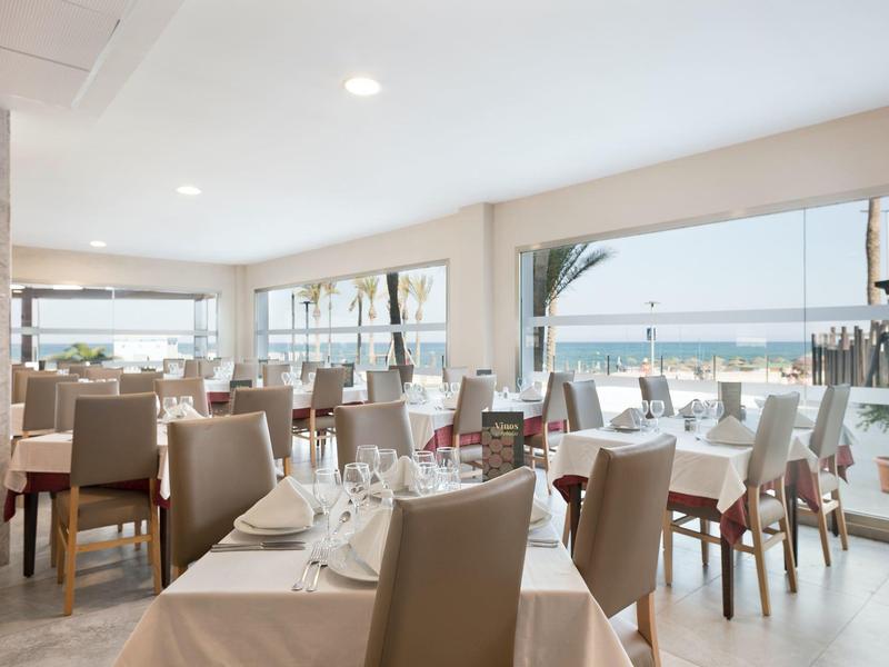 Helles Restaurant mit Tischdecken, bequemen Stühlen und großen Fenstern mit Meeresblick.