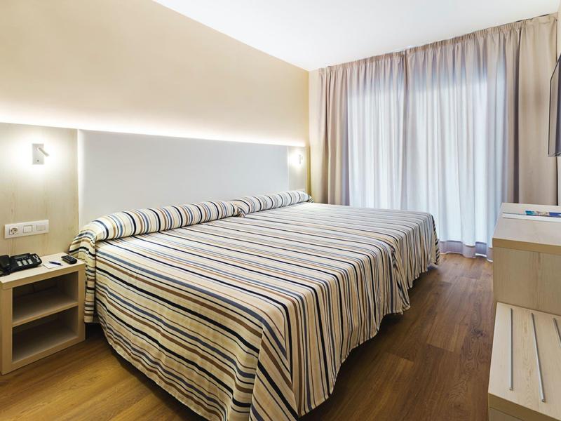 Modernes Schlafzimmer mit Doppelbett, Streifenbettwäsche, Holzfußboden und hellem Vorhang.