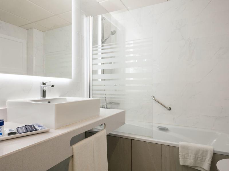 Helles Bad mit rechteckigem Waschbecken, großer Spiegel mit LED-Beleuchtung und Badewanne mit Griff.