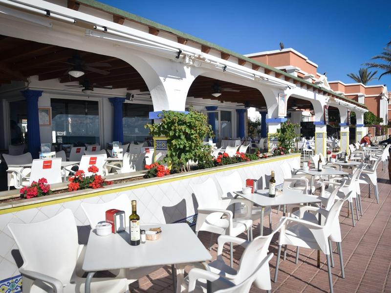 Freiluftcafé mit weißen Tischen und Stühlen, blauen Wänden und bogenförmigen Säulen.