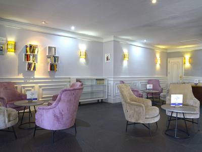 Nowoczesna część wypoczynkowa hotelu z pastelowymi fotelami i minimalistycznym wystrojem.