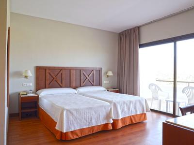 Hell eingerichtetes Doppelzimmer mit zwei Einzelbetten, Holzboden, Nachttischen und großer Fensterfront.