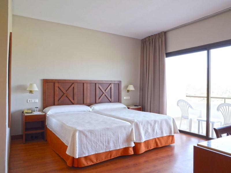 Hell eingerichtetes Doppelzimmer mit zwei Einzelbetten, Holzboden, Nachttischen und großer Fensterfront.