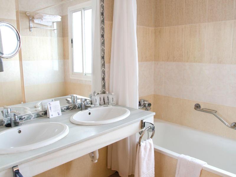 Helles Badezimmer mit Doppelwaschbecken, großer Spiegel, Badewanne und hellbeigen Fliesen.