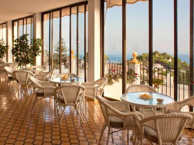 Sala colazioni luminosa con sedie in vimini e grandi finestre con vista sul mare.
