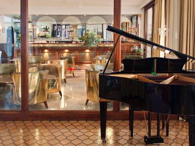 Elegante pianoforte nero nella hall dell'hotel con bar e posti a sedere sullo sfondo.