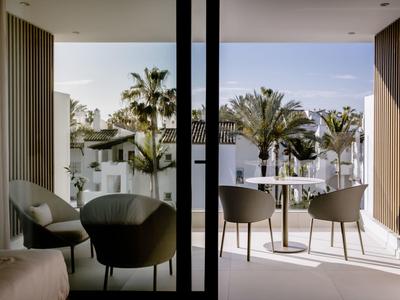 Balkon mit modernem Sitzbereich, weißen Häusern und Palmen im sonnigen Mittelmeerstil.