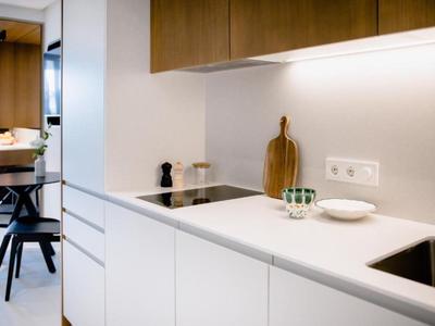 Moderne weiße Küche mit Holzschränken, elektrischem Herd, Spüle und schlichter Dekoration.