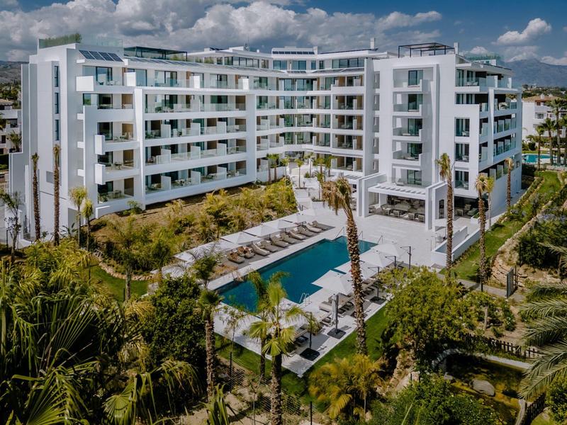 Modernes weißes Wohngebäude mit mehreren Etagen, Pool und grüner Gartenanlage im Vordergrund.