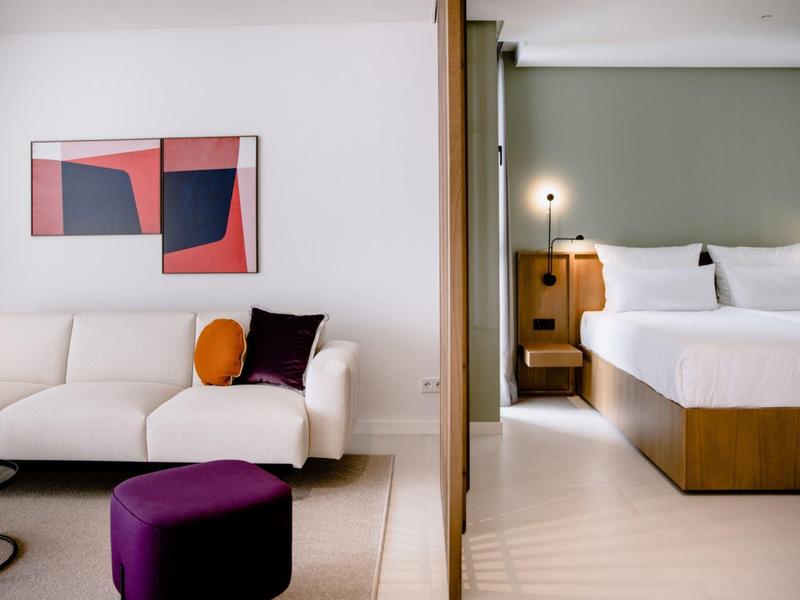 Modernes Schlafzimmer und Wohnzimmer mit weißem Sofa, lila Hocker und abstrakter Kunst an der Wand.