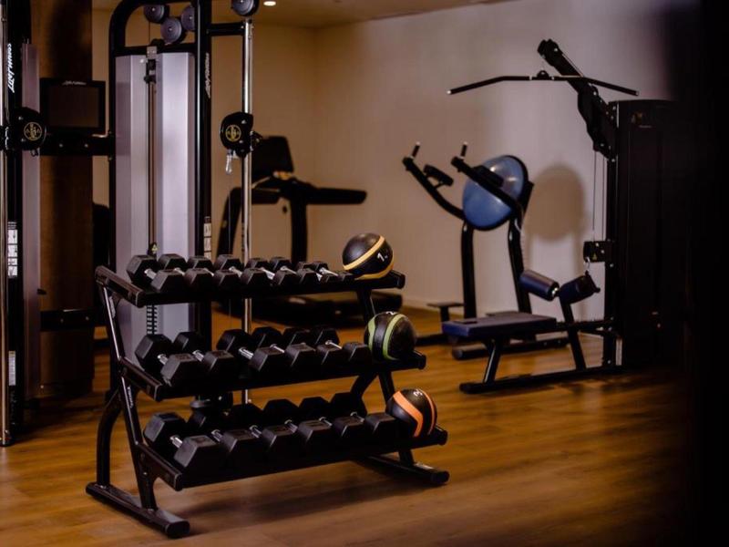 Fitnessraum mit Hanteln auf einem Ständer und mehreren Trainingsmaschinen, Holzfußboden, warme Beleuchtung.