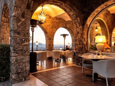 Przytulny taras restauracyjny z kamiennymi kolumnami i widokiem na krajobraz o zachodzie słońca.