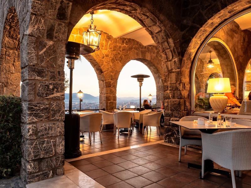 Gemütliche Terrasse eines Hotels mit antiken Steinbögen und Tischen mit Stühlen bei Dämmerung.