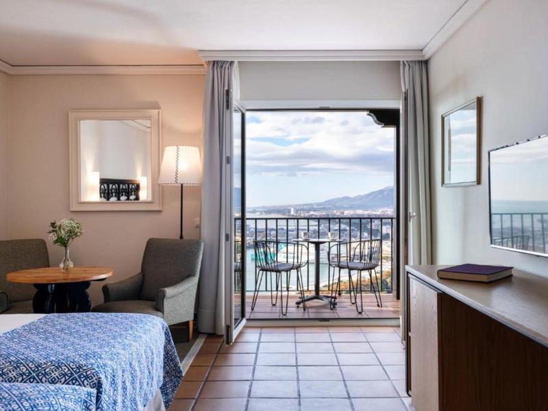 Helles Hotelzimmer mit Balkon, Kleiderschrank, Tisch, Stühlen und Blick auf das Meer.