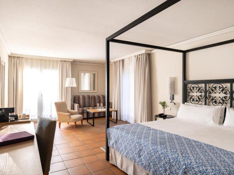 Helles Hotelzimmer mit Himmelbett, Schreibtisch und Sitzbereich mit Sofas.