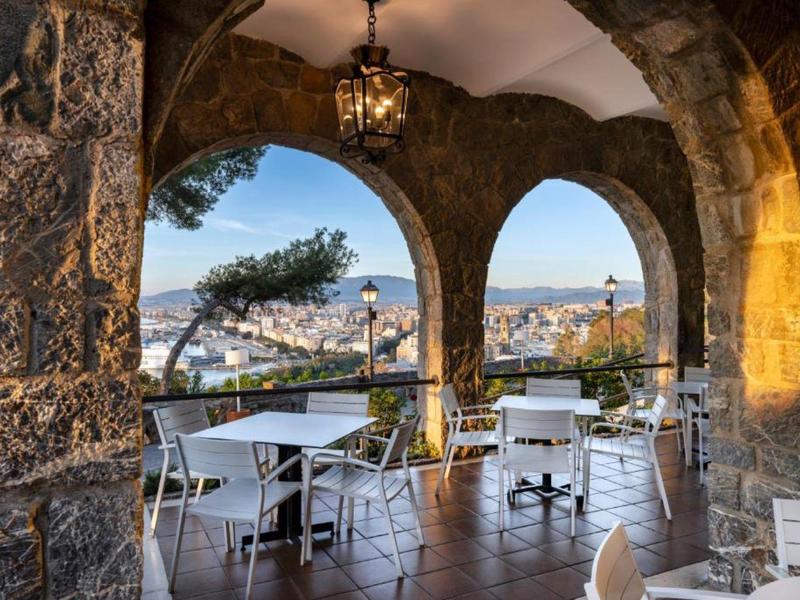 Überdachte Terrasse mit Bogengängen, weißen Tischen und Stühlen mit Blick auf die Stadt.