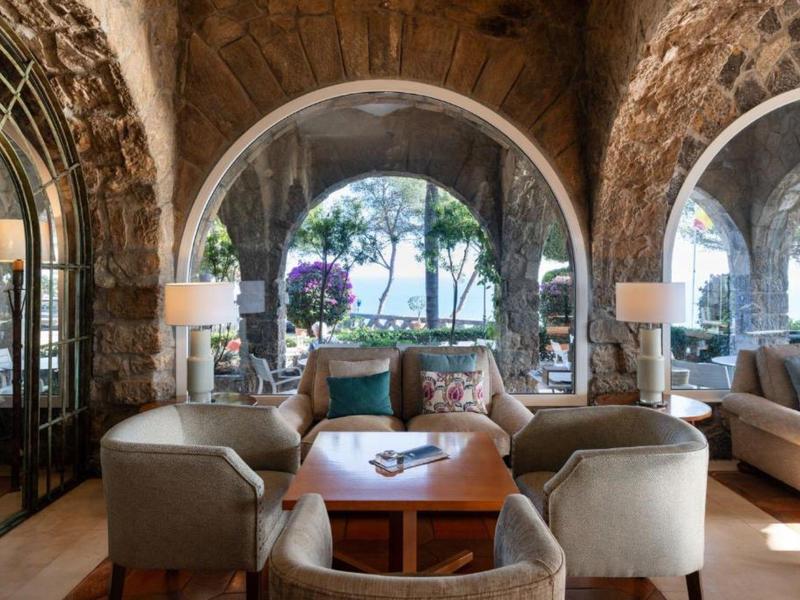 Gemütlicher Sitzbereich mit Sofas und Sesseln in einem Steingewölbe mit Blick auf die Natur.