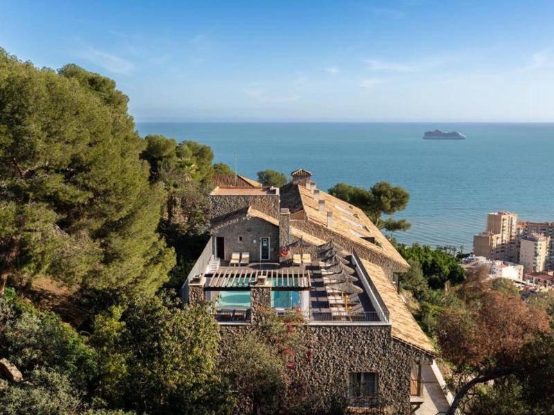 Blick auf ein Gebäude mit Pool, umgeben von Bäumen, mit Meer und Schiff im Hintergrund