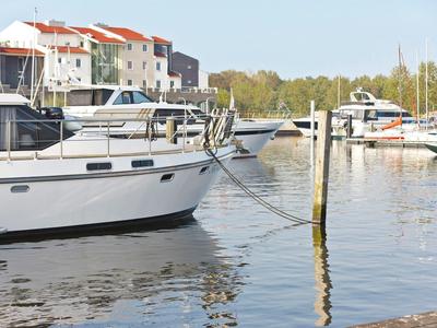 Weiße Boote liegen an Stegen im Hafen vor bunten Häusern und grünem Hintergrund.
