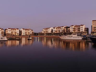 Hafen mit Booten und modernen Wohngebäuden bei Abenddämmerung, ruhiges Wasser spiegelt Gebäude.