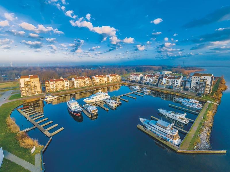 Moderne Wohngebäude mit Bootsstegen an ruhigem Wasser unter blauem Himmel und Wolken.