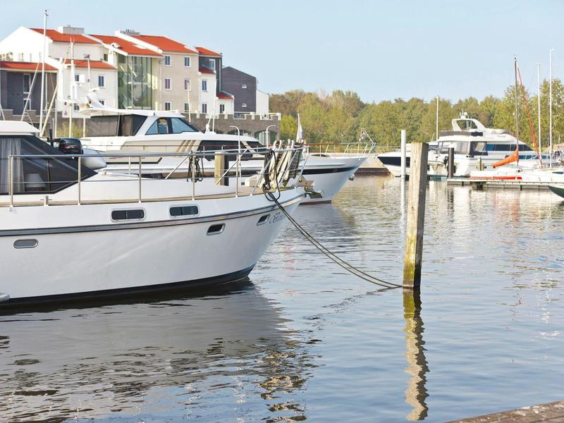 Weiße Boote liegen an Stegen im Hafen vor bunten Häusern und grünem Hintergrund.