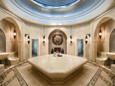 Luxuriöses Hammam mit Marmorflecken, Rundbecken und kunstvollen Wandlampen in warmem Licht.