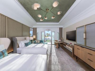 Helles Hotelzimmer mit zwei Betten, modernem Mobiliar und Balkon mit Blick auf das Meer.