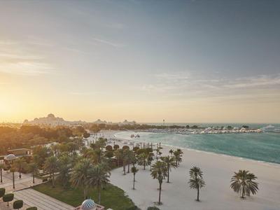 Sonnenaufgang über einem ruhigen Strand mit Palmen und einem Hotel im Hintergrund.