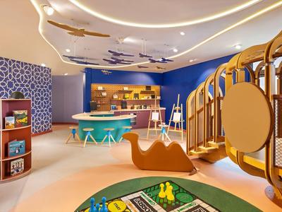 Bunter Kinderspielraum mit Rutsche, Sitzgelegenheiten und Spielecke in warmem Licht.