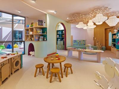 Bunter Kinderspielraum mit Tischen, Hockern, Kissen und dekorativen Wolken an der Decke.