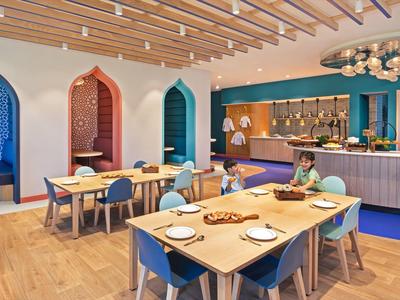 Moderner Speisesaal mit Holzböden, bunten Bögen und elegant gedeckten Tischen.